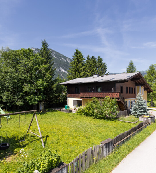 Außenansicht der Wohngemeinschaft mit Garten, Schaukel und einigen Bäumen.