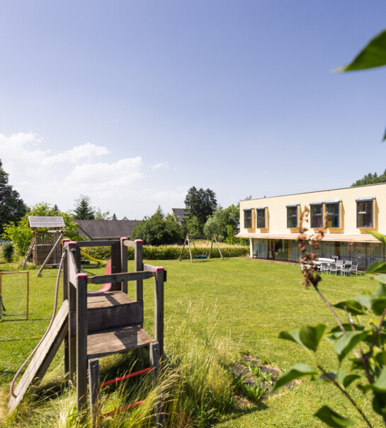 Außenansicht der Wohngemeinschaft mit Garten und Rutsche.