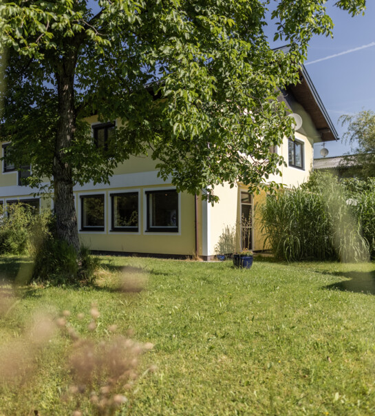 Außenansicht der Wohngemeinschaft mit Garten und einem Baum.