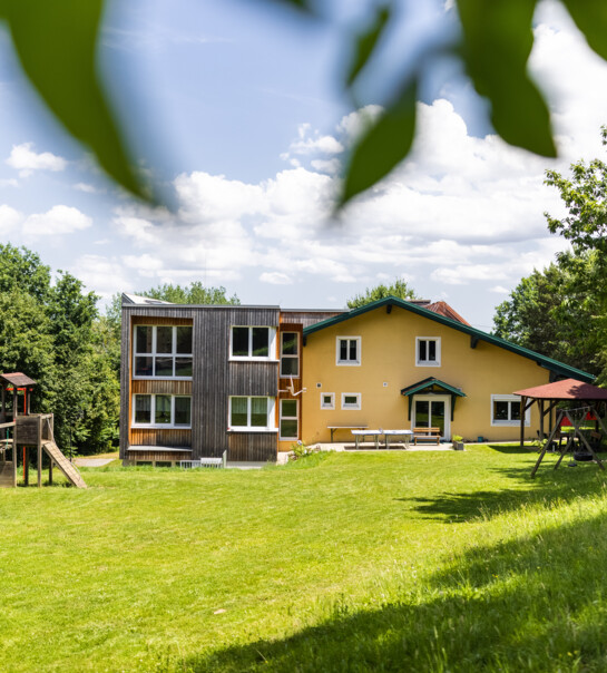 Außenansicht der Wohngemeinschaft mit Garten, Spielturm und Schaukel.