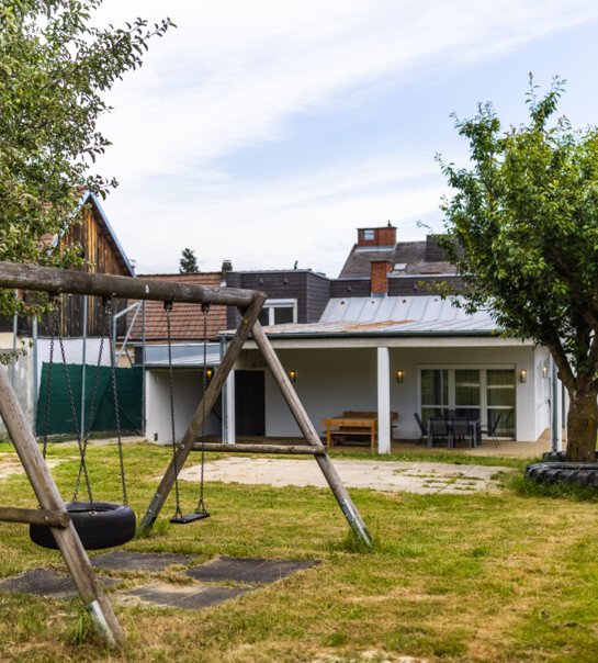 Außenansicht der Wohngemeinschaft mit Garten Schaukel, und überdachtem Essbereich.