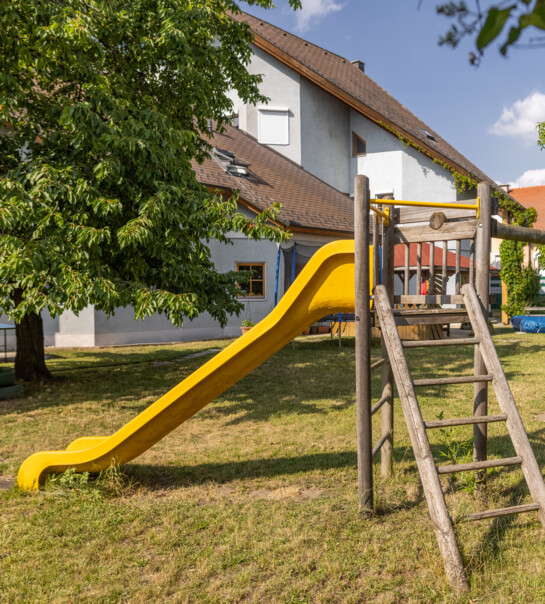 Außenansicht der Wohngemeinschaft mit Garten, Holzgestell und Rutsche.